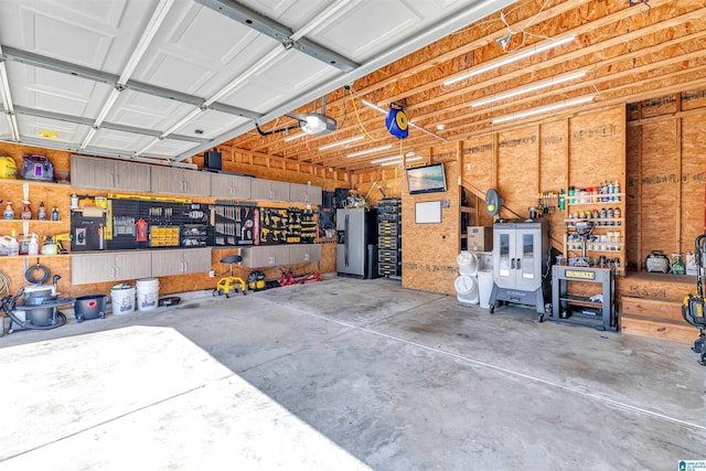 garage with a workshop area, a garage door opener, and stainless steel fridge with ice dispenser