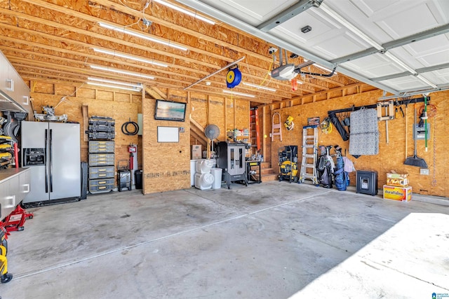 garage featuring a workshop area, a garage door opener, and stainless steel refrigerator with ice dispenser