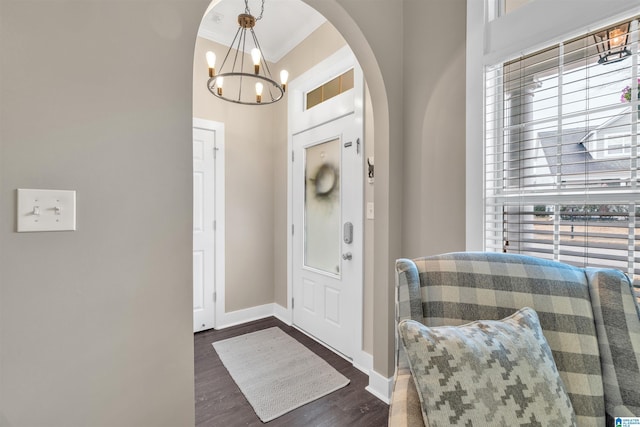 entrance foyer with crown molding, baseboards, a chandelier, dark wood finished floors, and arched walkways