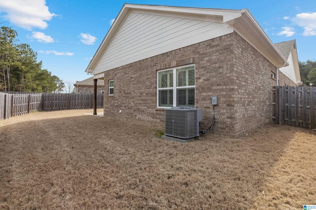 view of side of property featuring brick siding, a lawn, cooling unit, and a fenced backyard