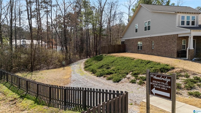 view of side of property featuring brick siding, gravel driveway, and fence