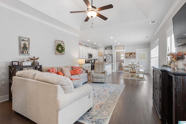 living area featuring visible vents, crown molding, dark wood finished floors, a tray ceiling, and a ceiling fan