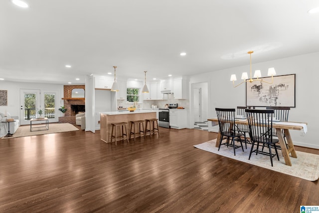 dining area with a brick fireplace, baseboards, dark wood finished floors, a chandelier, and recessed lighting