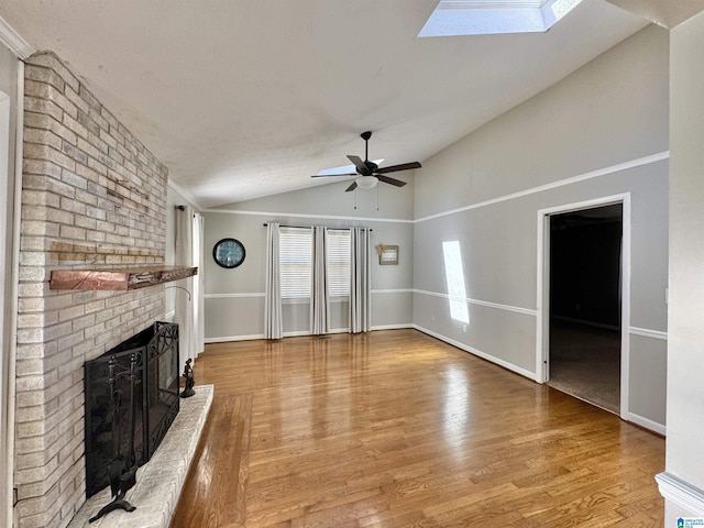 unfurnished living room featuring vaulted ceiling with skylight, a fireplace, light wood-style floors, and ceiling fan