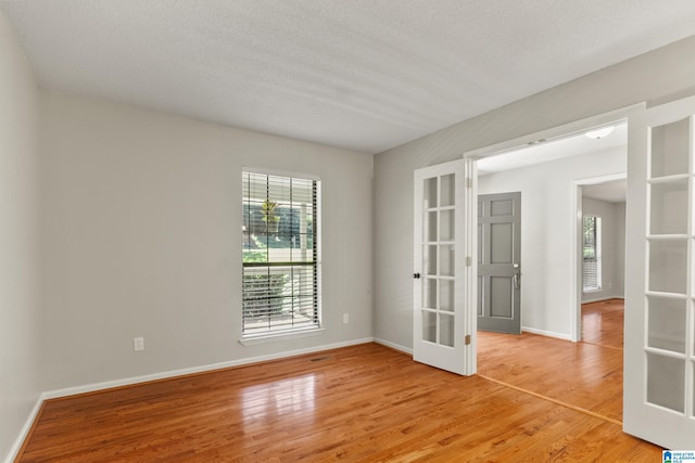 unfurnished room with a healthy amount of sunlight, light wood-style floors, and french doors