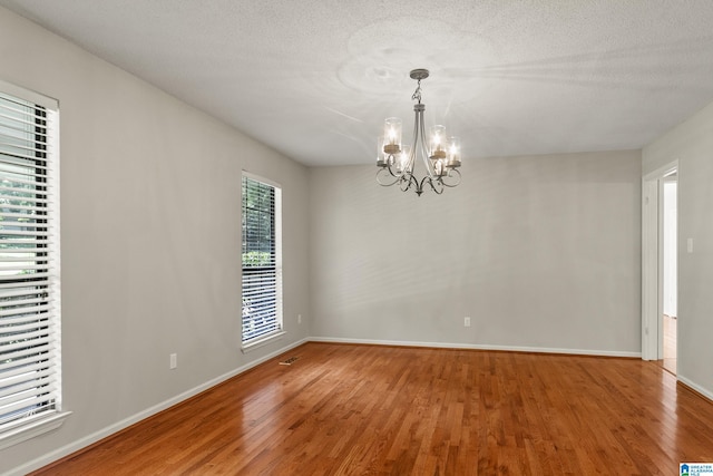 empty room featuring a textured ceiling, wood finished floors, baseboards, and a chandelier