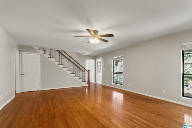 unfurnished living room featuring stairs, wood finished floors, baseboards, and a ceiling fan