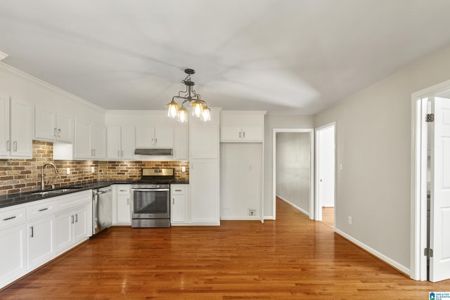 kitchen featuring dark countertops, under cabinet range hood, white cabinets, stainless steel appliances, and a sink