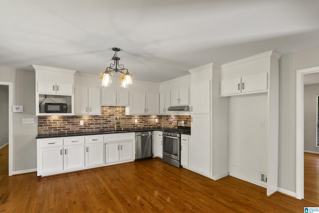 kitchen with dark countertops, white cabinets, under cabinet range hood, and stainless steel appliances