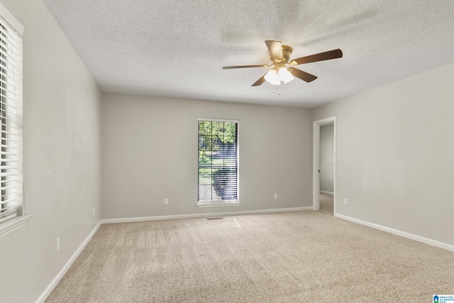 spare room featuring a textured ceiling, light colored carpet, baseboards, and ceiling fan