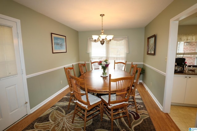 dining room with light wood-type flooring, baseboards, and an inviting chandelier