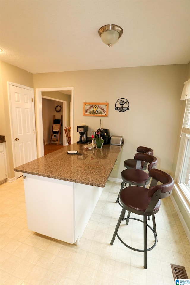 kitchen with visible vents, dark stone countertops, white cabinetry, a peninsula, and baseboards