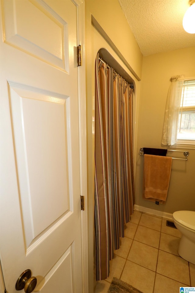 bathroom with baseboards, visible vents, tile patterned flooring, a textured ceiling, and toilet