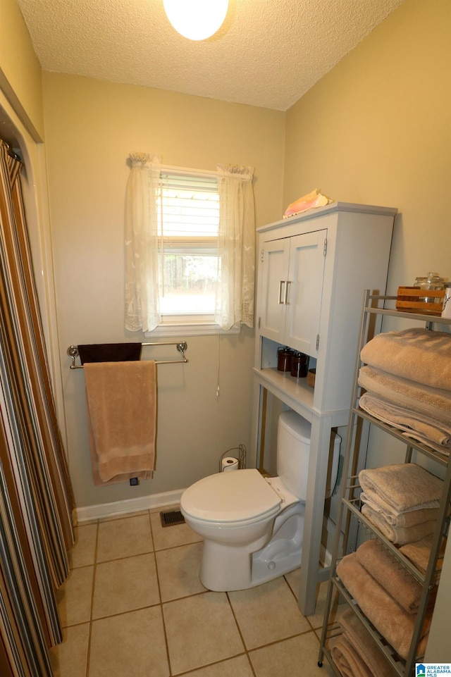 bathroom with a textured ceiling, visible vents, toilet, and tile patterned flooring