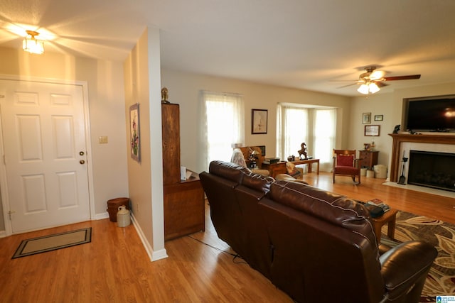 living area featuring ceiling fan, baseboards, a fireplace with flush hearth, and wood finished floors