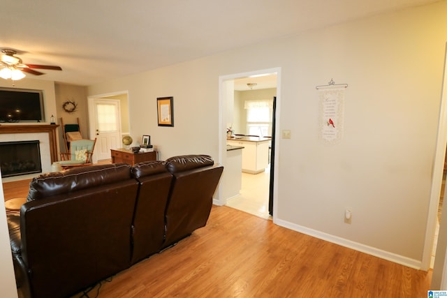 living area with ceiling fan, a fireplace, baseboards, and light wood-style floors