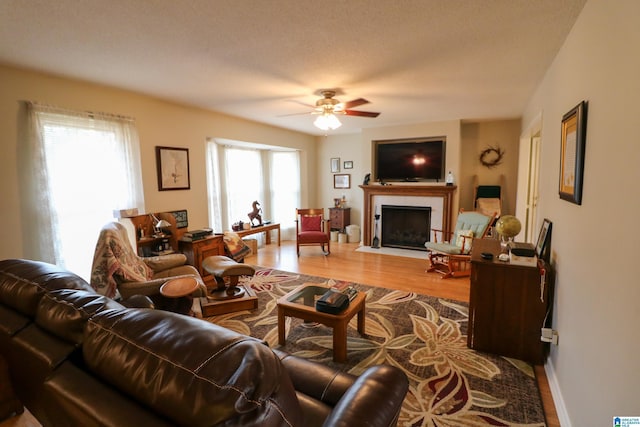 living room featuring light wood-type flooring, a fireplace with flush hearth, baseboards, and ceiling fan