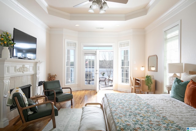 bedroom featuring a tray ceiling, wood finished floors, a tile fireplace, and access to outside