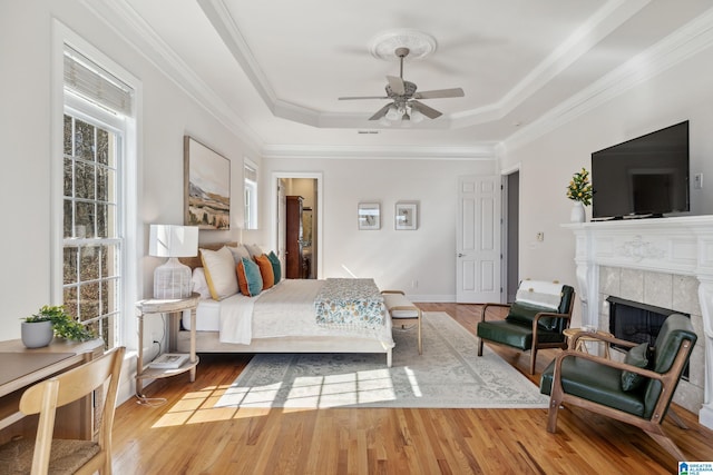 bedroom featuring a tray ceiling, wood finished floors, a fireplace, and crown molding