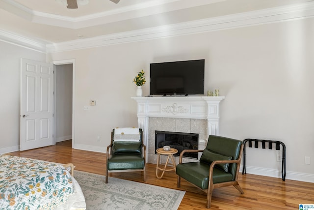 bedroom featuring a tiled fireplace, ornamental molding, baseboards, and wood finished floors