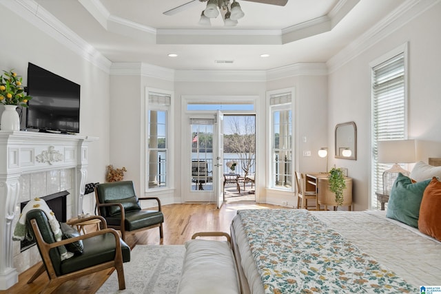 bedroom with a tiled fireplace, a tray ceiling, access to outside, and wood finished floors