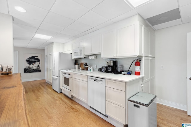 kitchen featuring light wood-type flooring, backsplash, white appliances, white cabinets, and light countertops