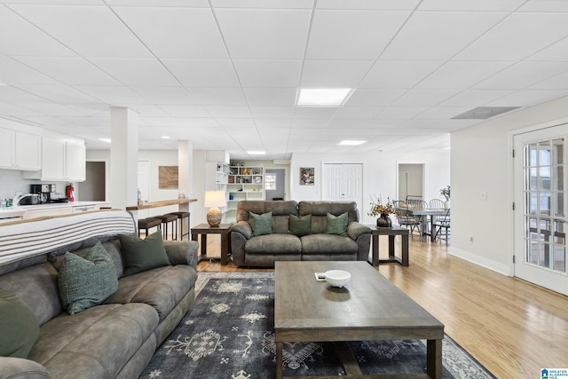 living area with a paneled ceiling, baseboards, and light wood finished floors