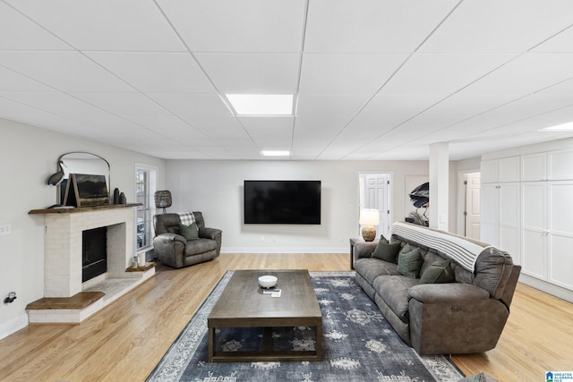 living area featuring wood finished floors, a fireplace, baseboards, and a paneled ceiling