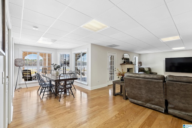 dining room with a fireplace, light wood-type flooring, a drop ceiling, and baseboards