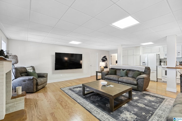 living area with a drop ceiling, baseboards, and light wood finished floors