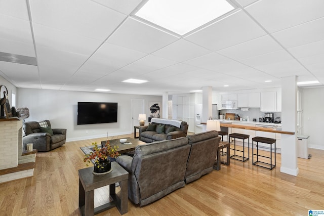 living area with light wood-style flooring, a paneled ceiling, and baseboards