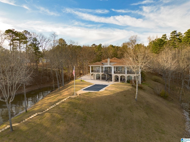 back of property featuring a yard, a patio, a wooded view, and a water view