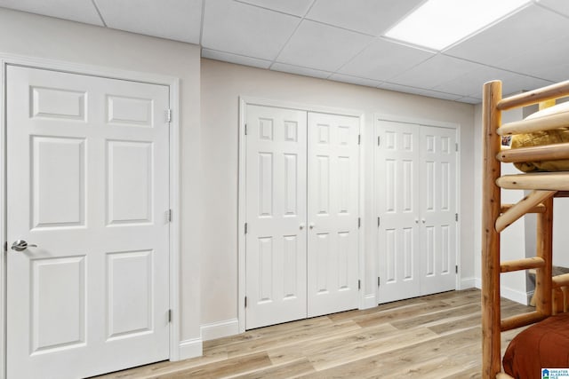 unfurnished bedroom with baseboards, two closets, light wood-type flooring, and a paneled ceiling