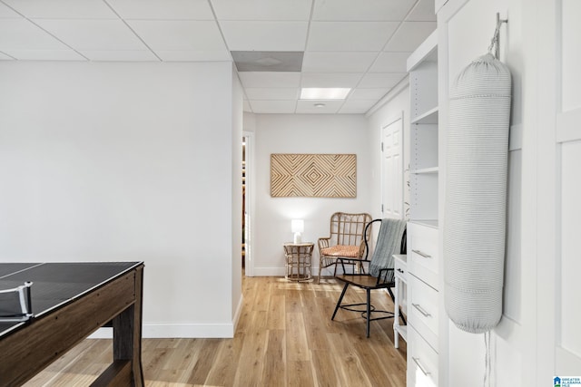 sitting room featuring a drop ceiling, baseboards, and light wood-style floors