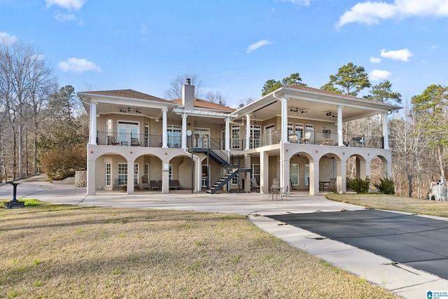 back of property with a balcony, a ceiling fan, a chimney, stucco siding, and a patio area