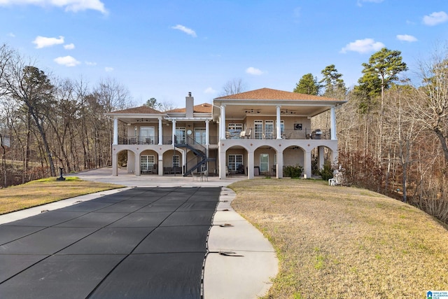 back of house with a balcony, a ceiling fan, a chimney, a patio area, and a lawn