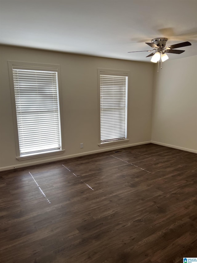 spare room with baseboards, dark wood finished floors, and a ceiling fan