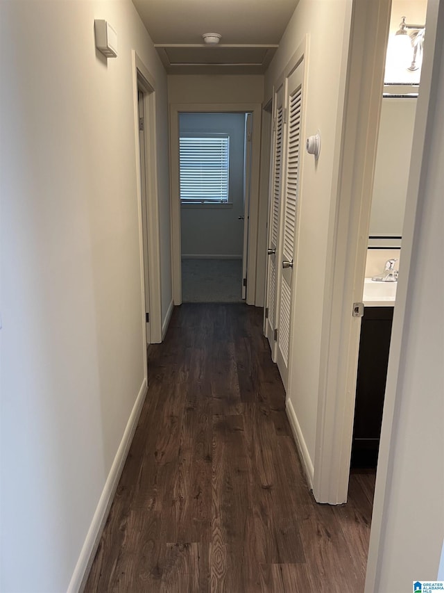 hallway with a sink, baseboards, and dark wood-style floors