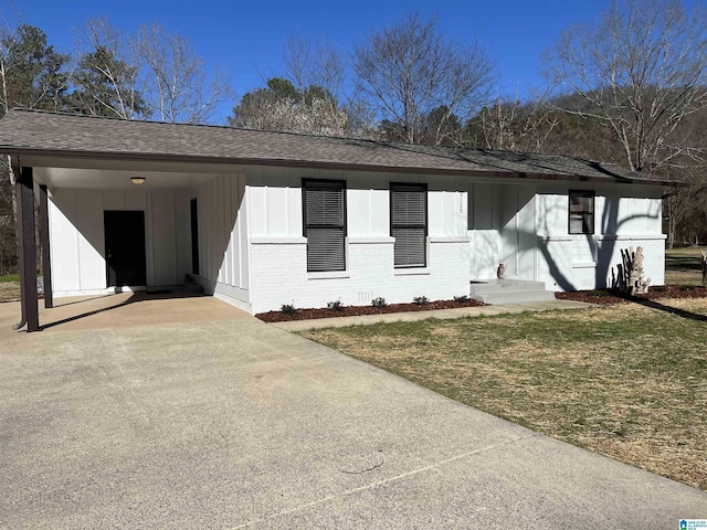 view of front facade with brick siding, board and batten siding, a front yard, roof with shingles, and driveway