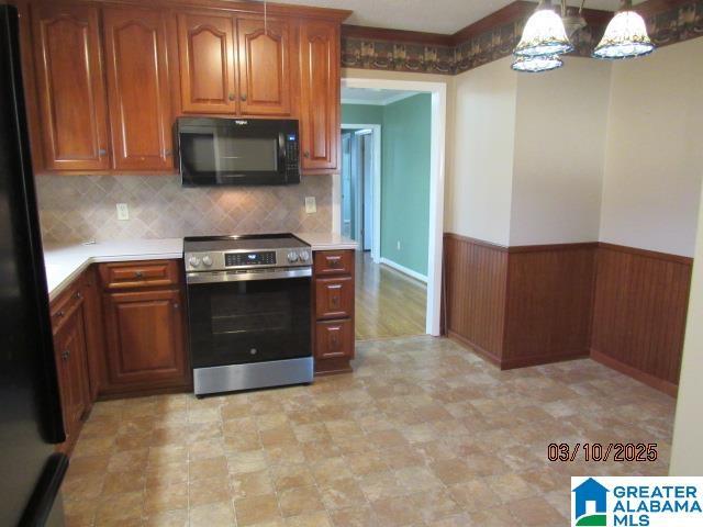 kitchen with wooden walls, a wainscoted wall, light countertops, brown cabinetry, and black appliances