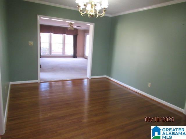 unfurnished room featuring ceiling fan with notable chandelier, wood finished floors, baseboards, and ornamental molding