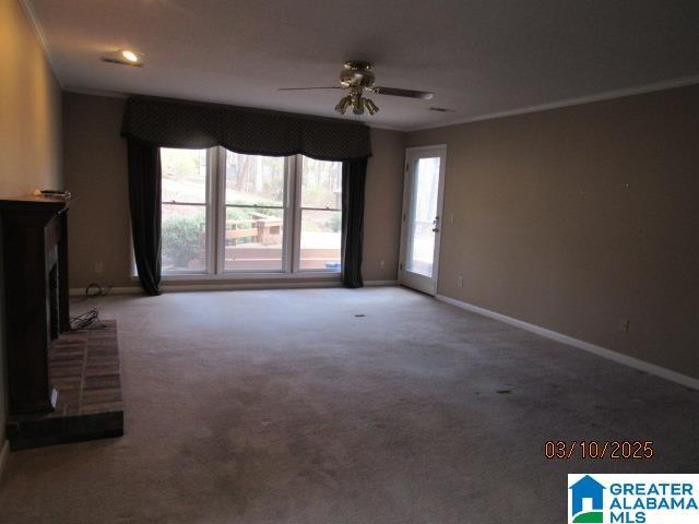 unfurnished living room with a ceiling fan, baseboards, carpet floors, ornamental molding, and a brick fireplace