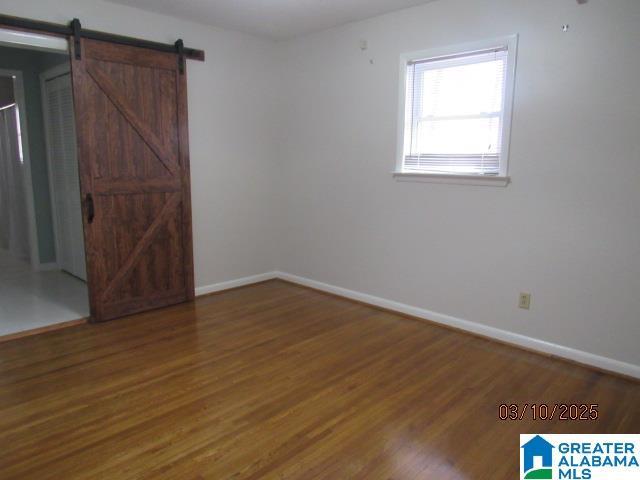 spare room featuring a barn door, baseboards, and wood finished floors