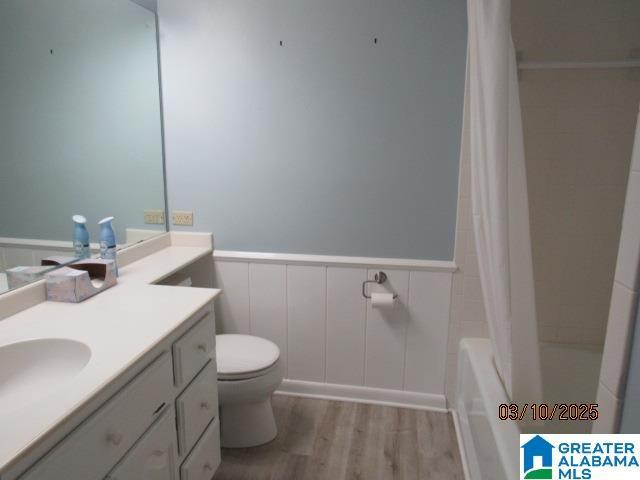 full bathroom featuring a wainscoted wall, toilet, shower / bath combo, wood finished floors, and vanity