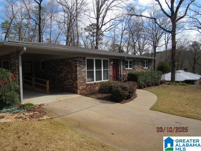 ranch-style home featuring an attached carport, a front yard, brick siding, and driveway