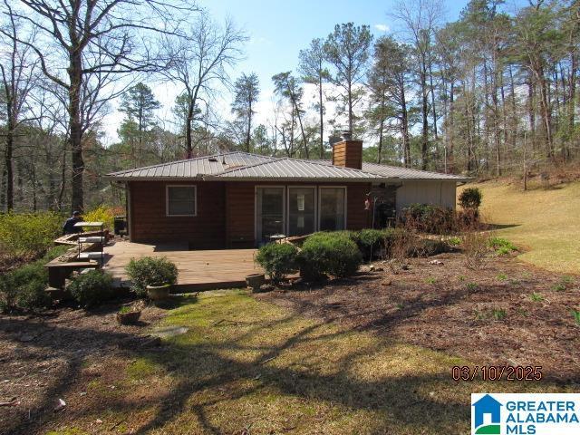 back of property featuring metal roof, a yard, a deck, and a chimney