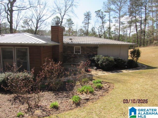 view of side of home with a yard, metal roof, a chimney, and a standing seam roof