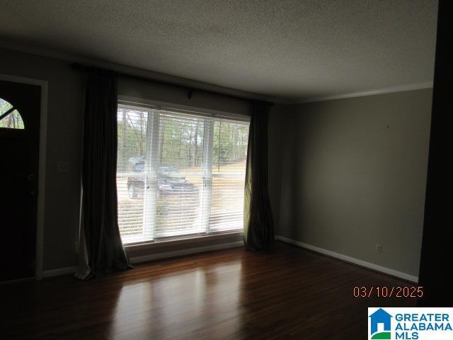 empty room with a textured ceiling, crown molding, baseboards, and wood finished floors