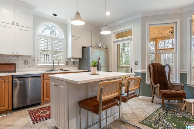 kitchen with a sink, appliances with stainless steel finishes, crown molding, light countertops, and decorative backsplash