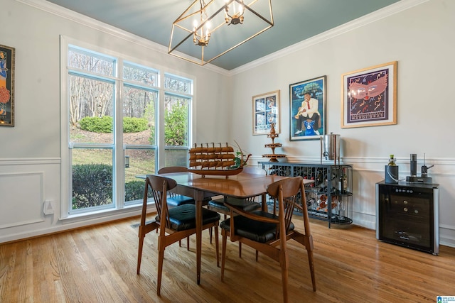 dining space with a chandelier, wood finished floors, ornamental molding, and wainscoting